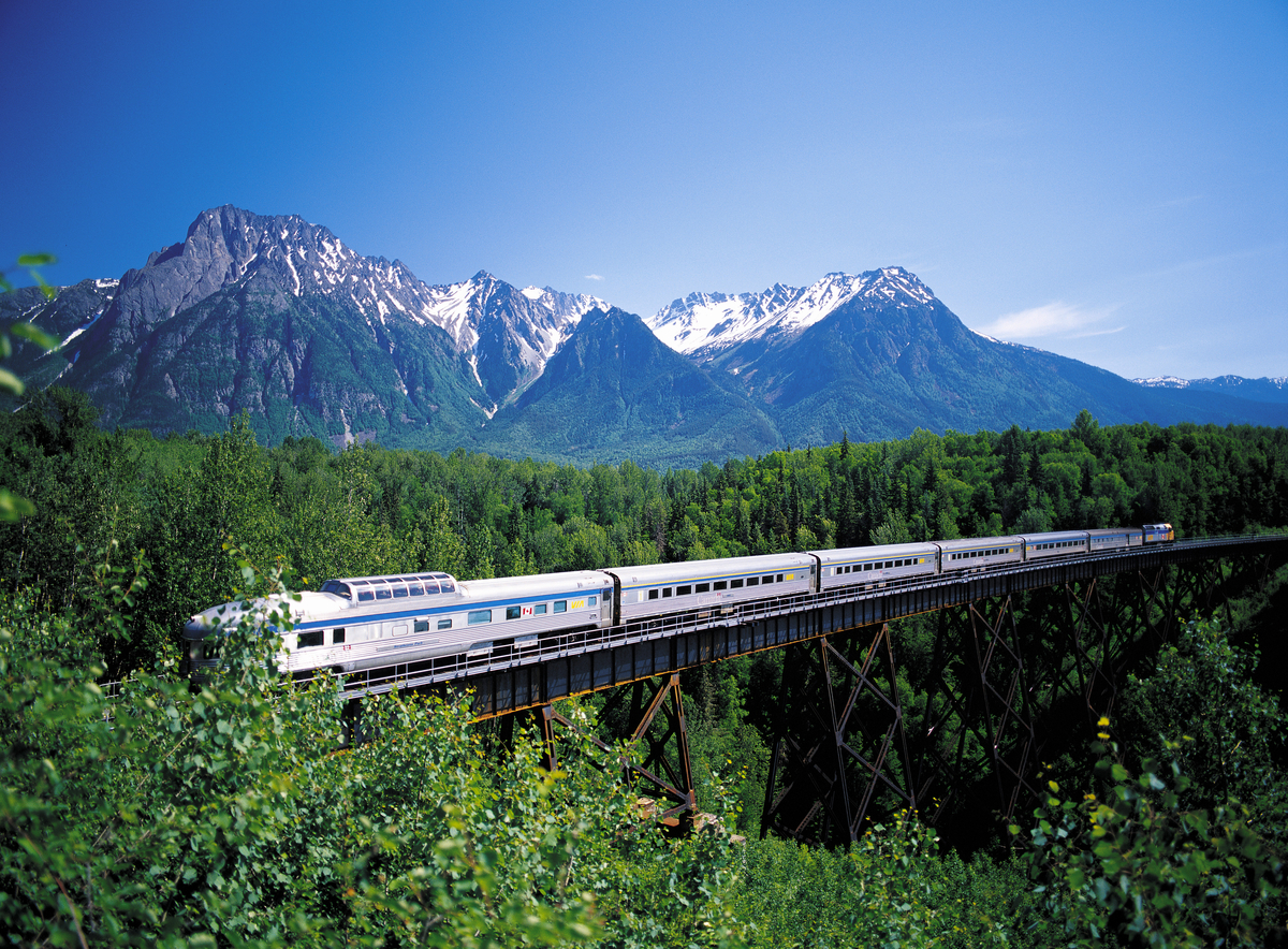 VIA Rail train going over the bridge through a forest in the mountains