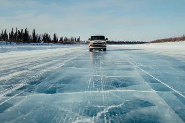 Car driving along the ice road near Yellowknife with snowy trees on each side