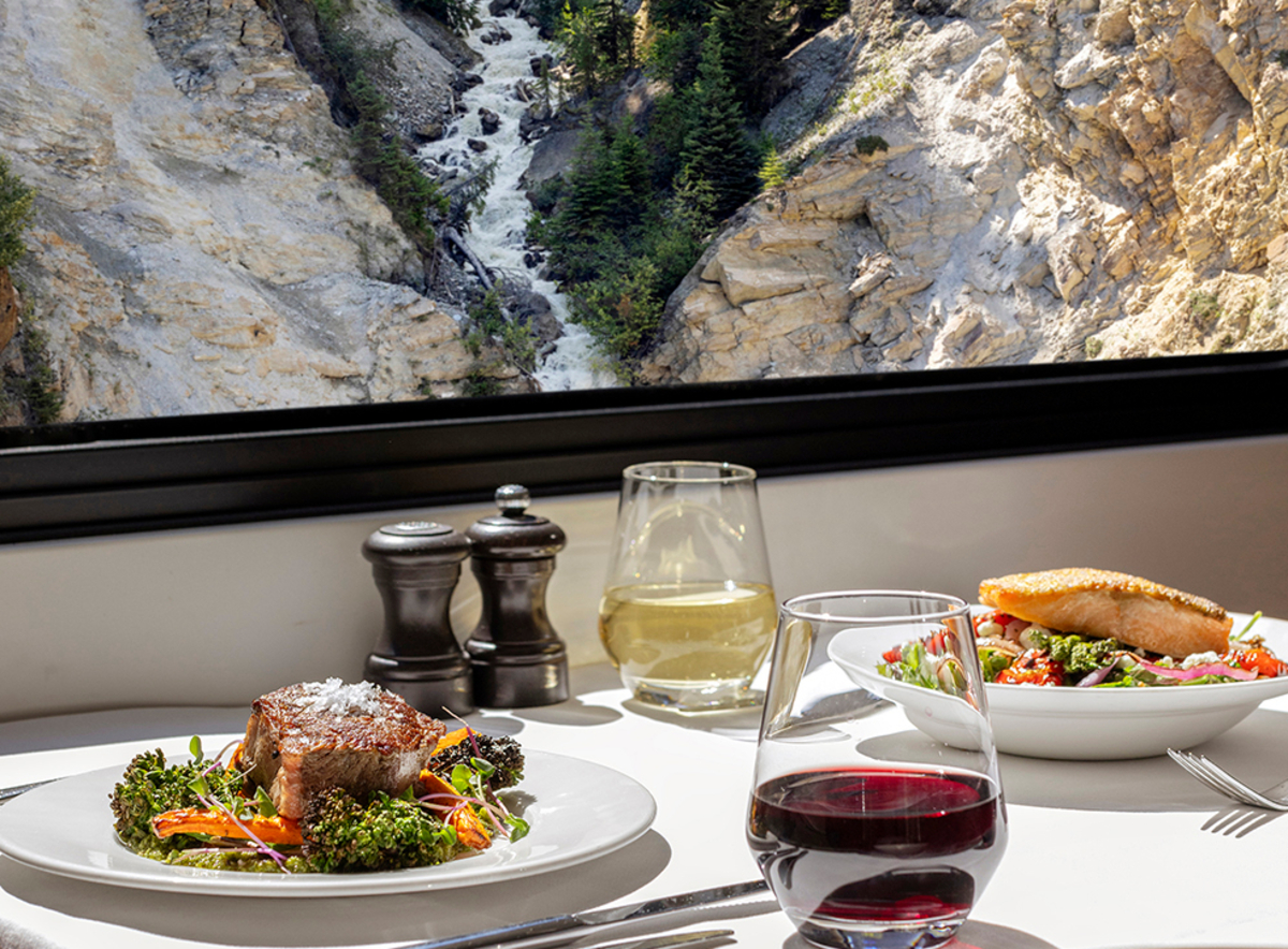 Lunch dishes and glasses of wine on a table next to a window in the Rocky Mountaineer GoldLeaf dining room 