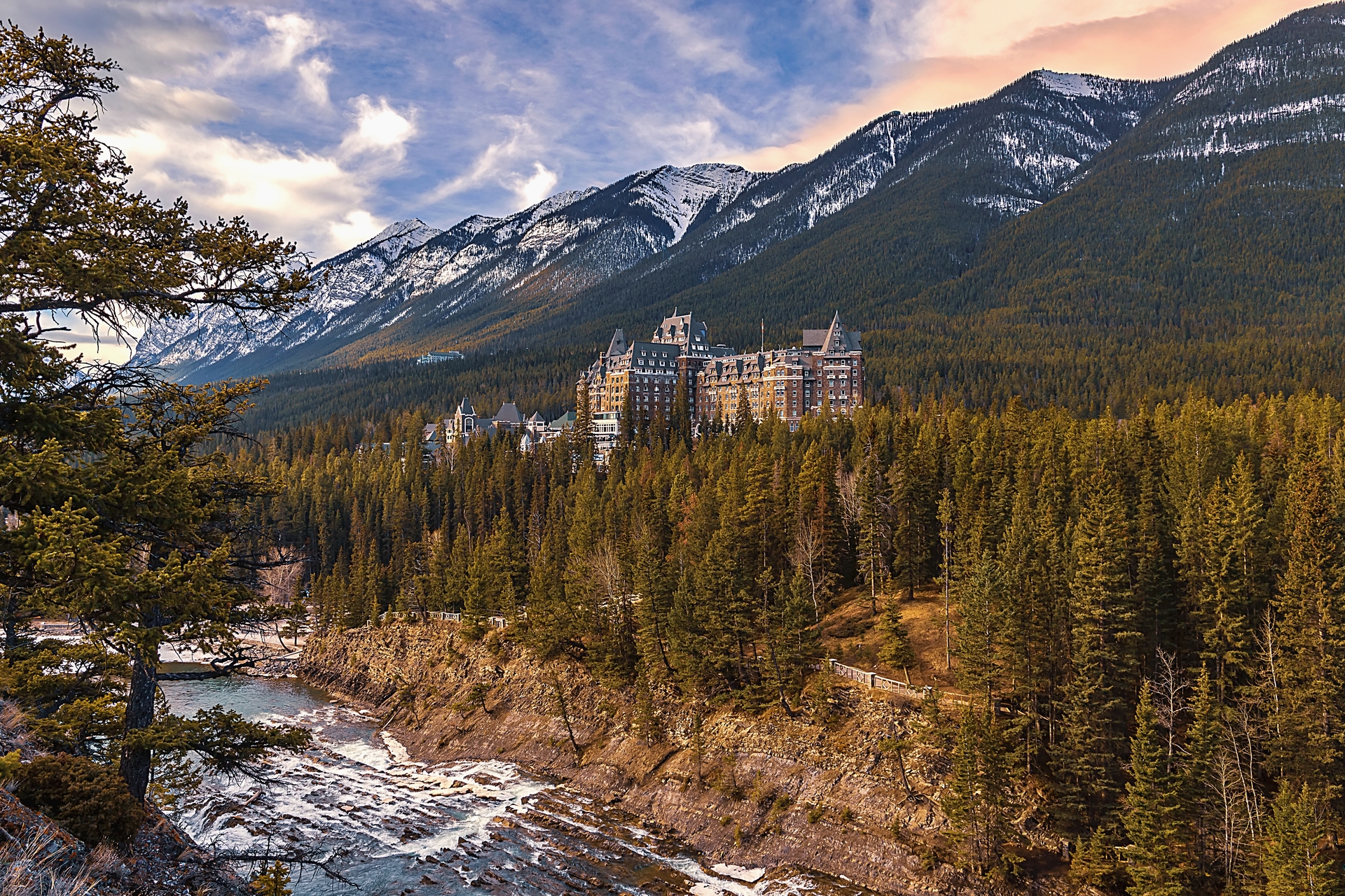 A panoramic view of a cloudy sunrise over mountains and forest by the Banff Springs Hotel.