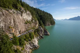 The Rocky Mountaineer train winds around cliffs on the Sea To Sky portion of the Rainforest to Gold Rush Route.