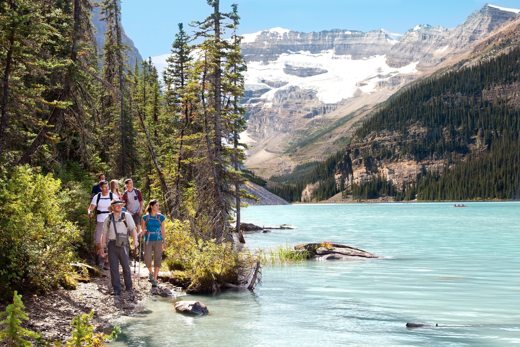 A guide leads a group of hikers along a trail beside the blue waters of Lake Louise