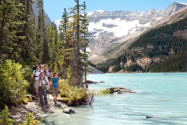 A guide leads a group of hikers along a trail beside the blue waters of Lake Louise