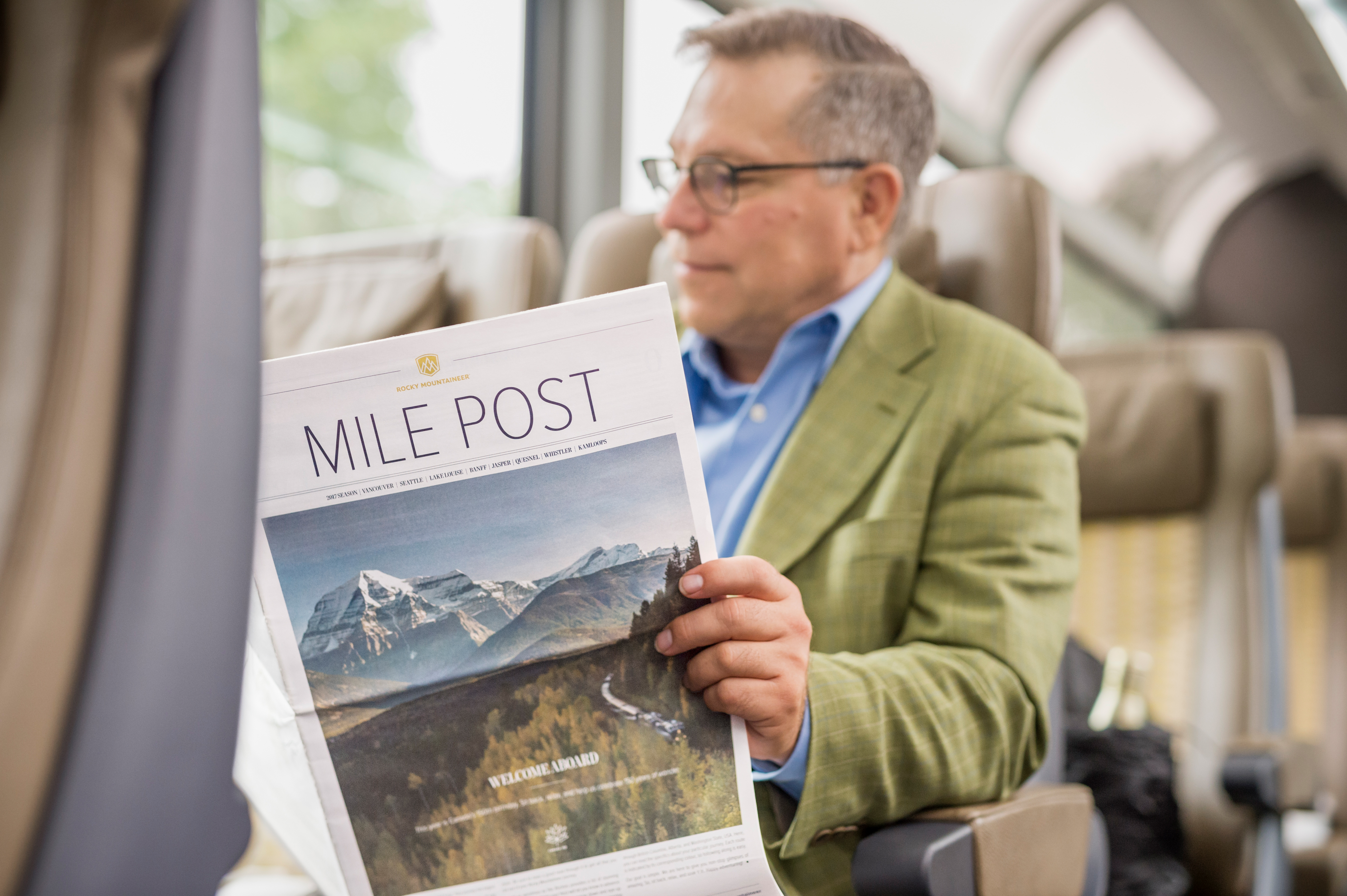Man reading Mile Post newspaper onboard Rocky Mountaineer in SilverLeaf service