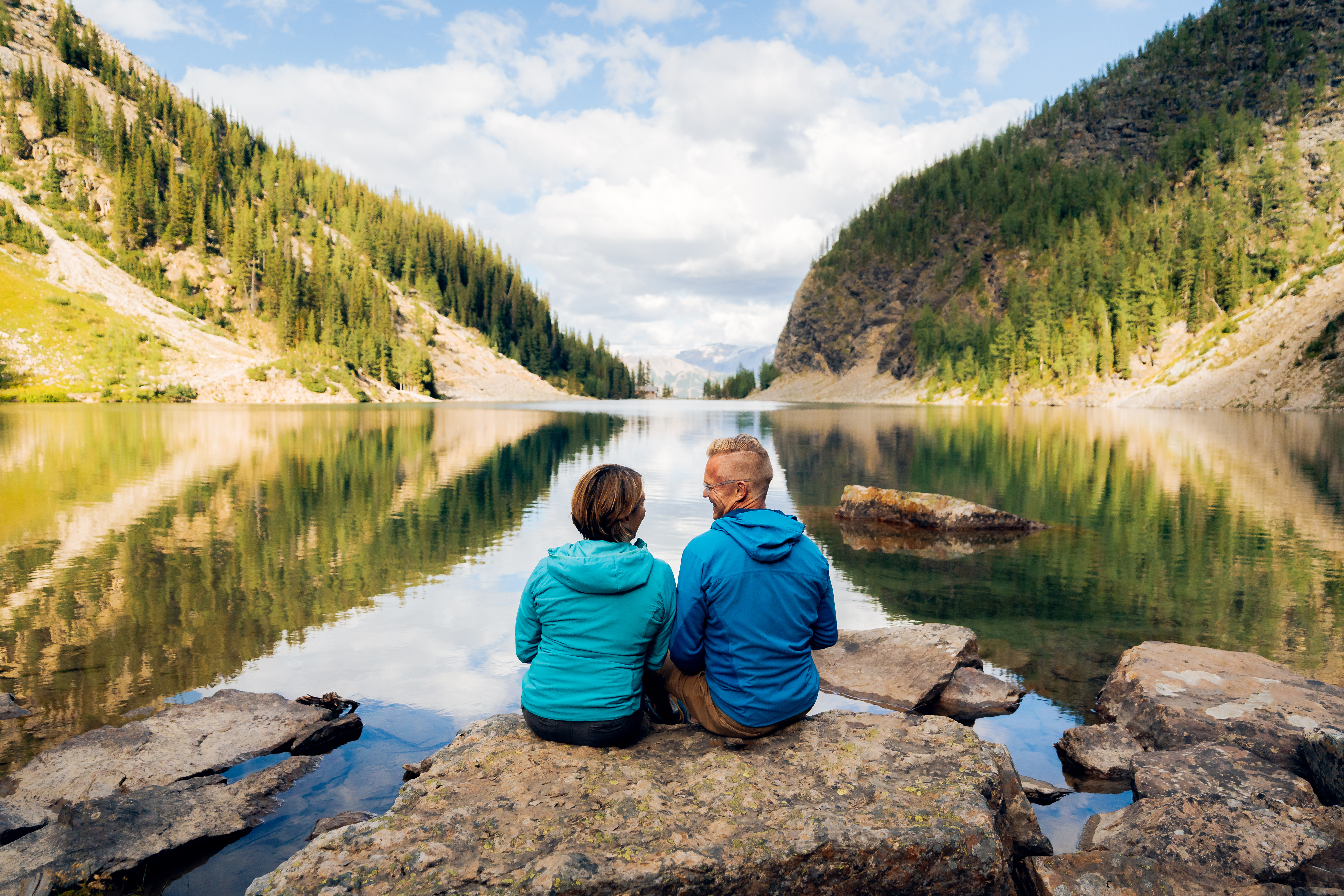 A couple sitting on a rock on the shore of Lake Agnes with mountains rising up on both sides