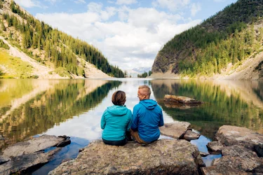 A couple sitting on a rock on the shore of Lake Agnes with mountains rising up on both sides