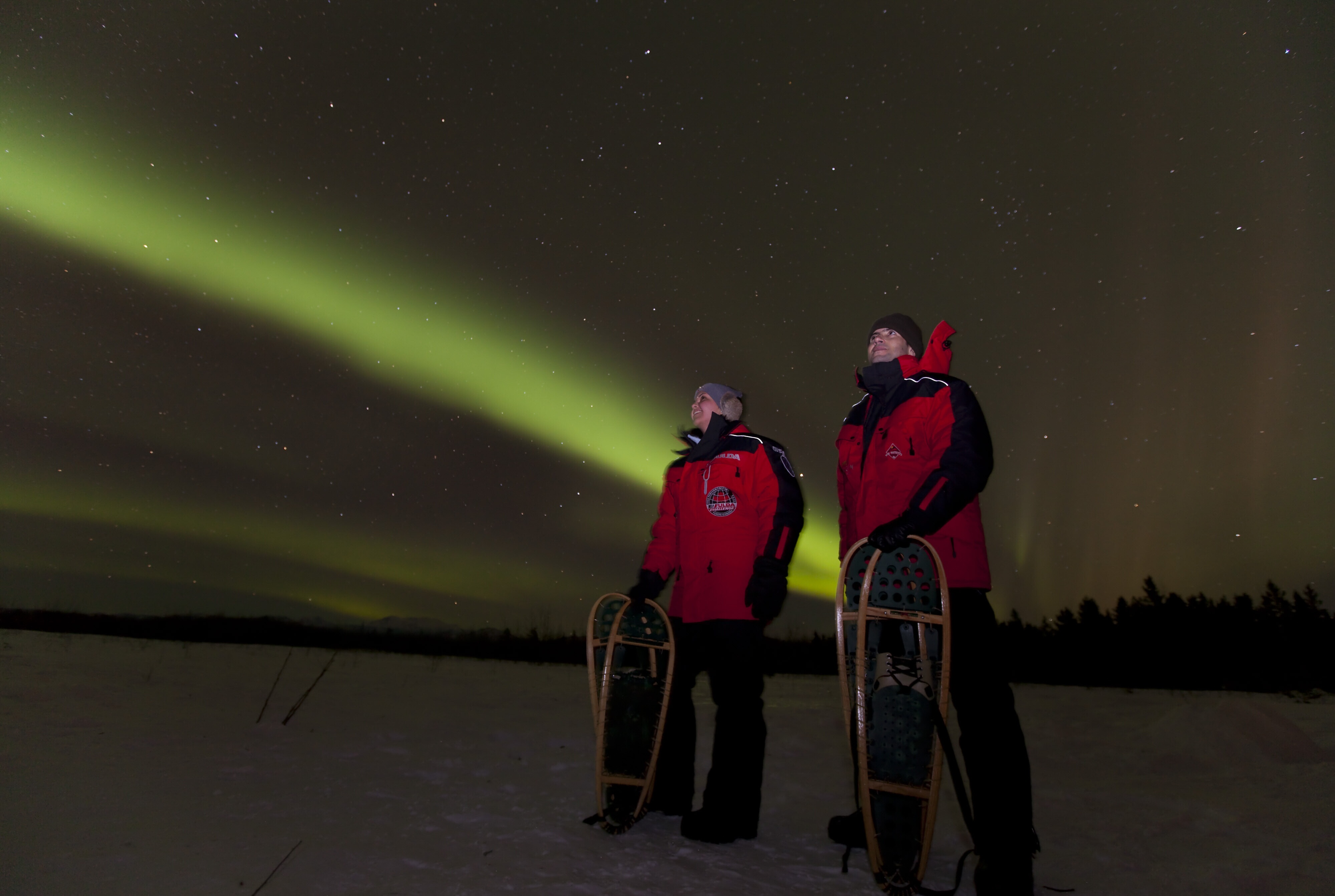 Two guests standing underneath the Northern Lights in the Yukon
