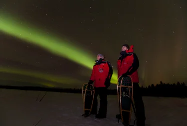 Two guests standing underneath the Northern Lights in the Yukon