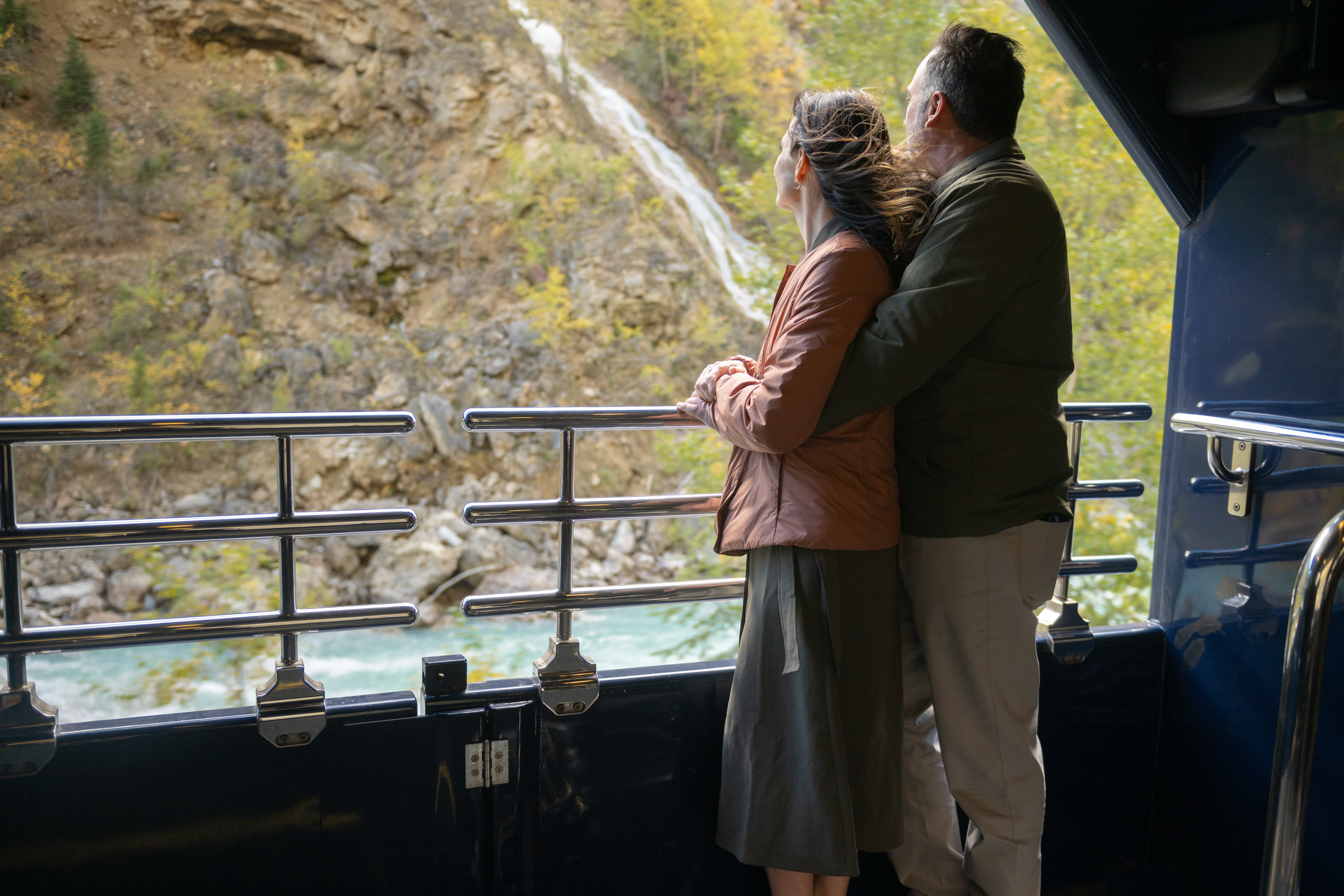 Guests looking at waterfall scenery from the GoldLeaf outdoor viewing platform on the Rocky Mountaineer Train