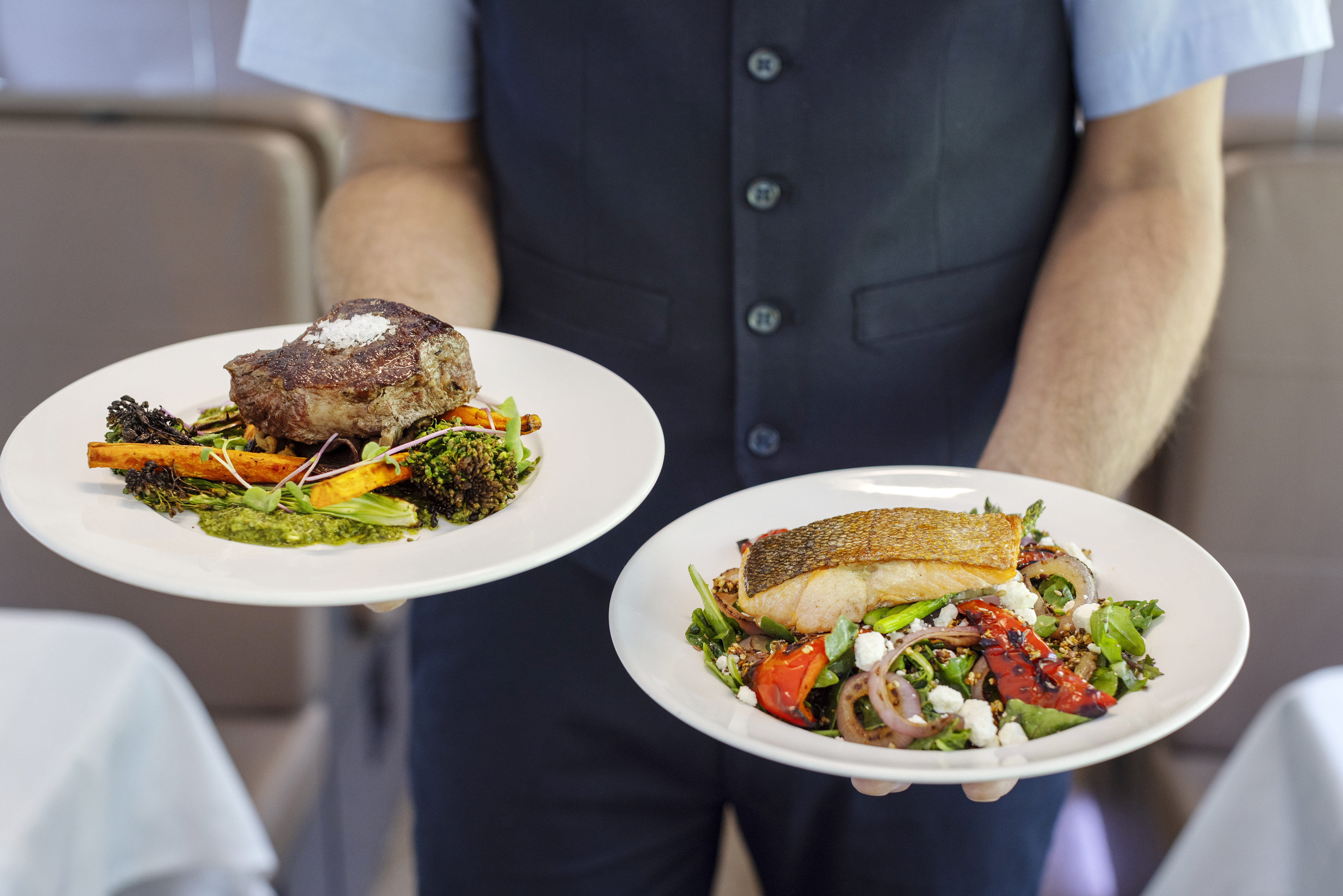Close up of Rocky Mountaineer host holding plates of Alberta Striploin Steak and Crispy Skin Lois Lake Steelhead