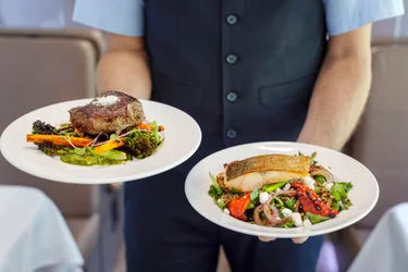Close up of Rocky Mountaineer host holding plates of Alberta Striploin Steak and Crispy Skin Lois Lake Steelhead