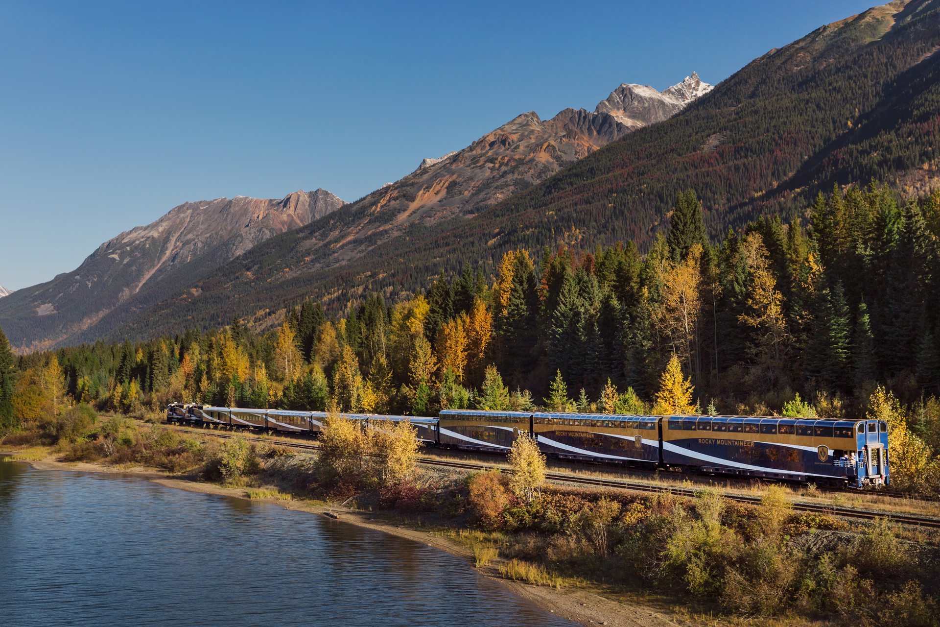 Rocky Mountaineer train travelling along the water on the Journey Through the Clouds Route.
