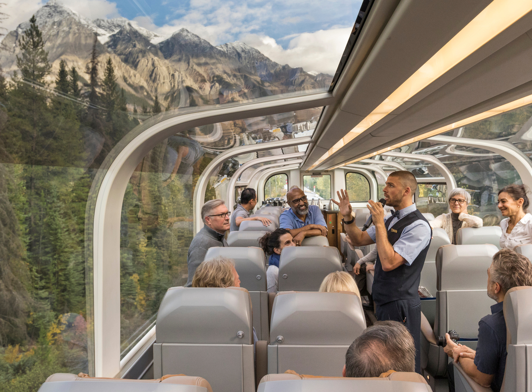 Host speaks to guests about the scenery as they look through the glass-dome windows in Rocky Mountaineer GoldLeaf service