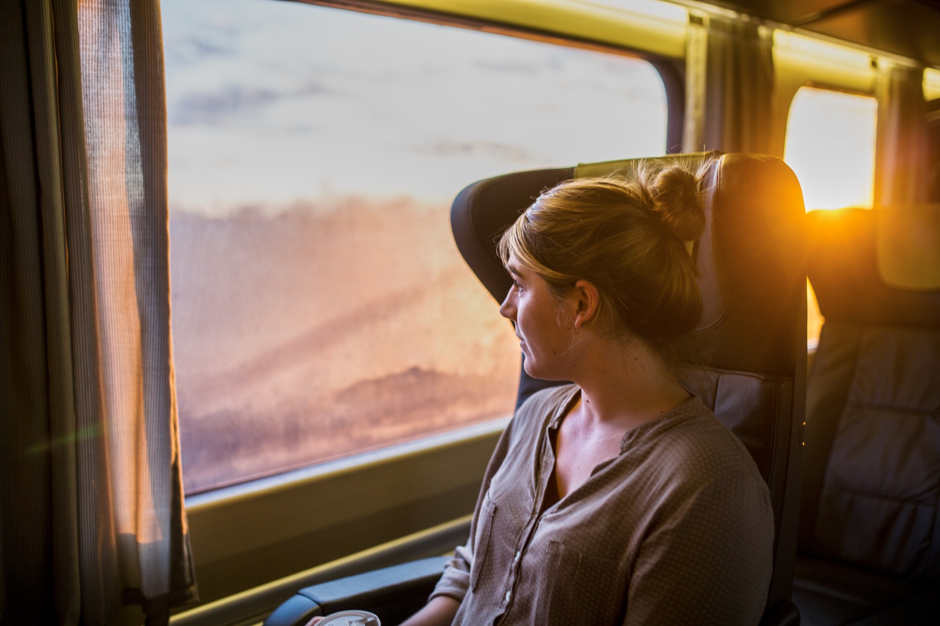 A woman looks out a train car window at sunset
