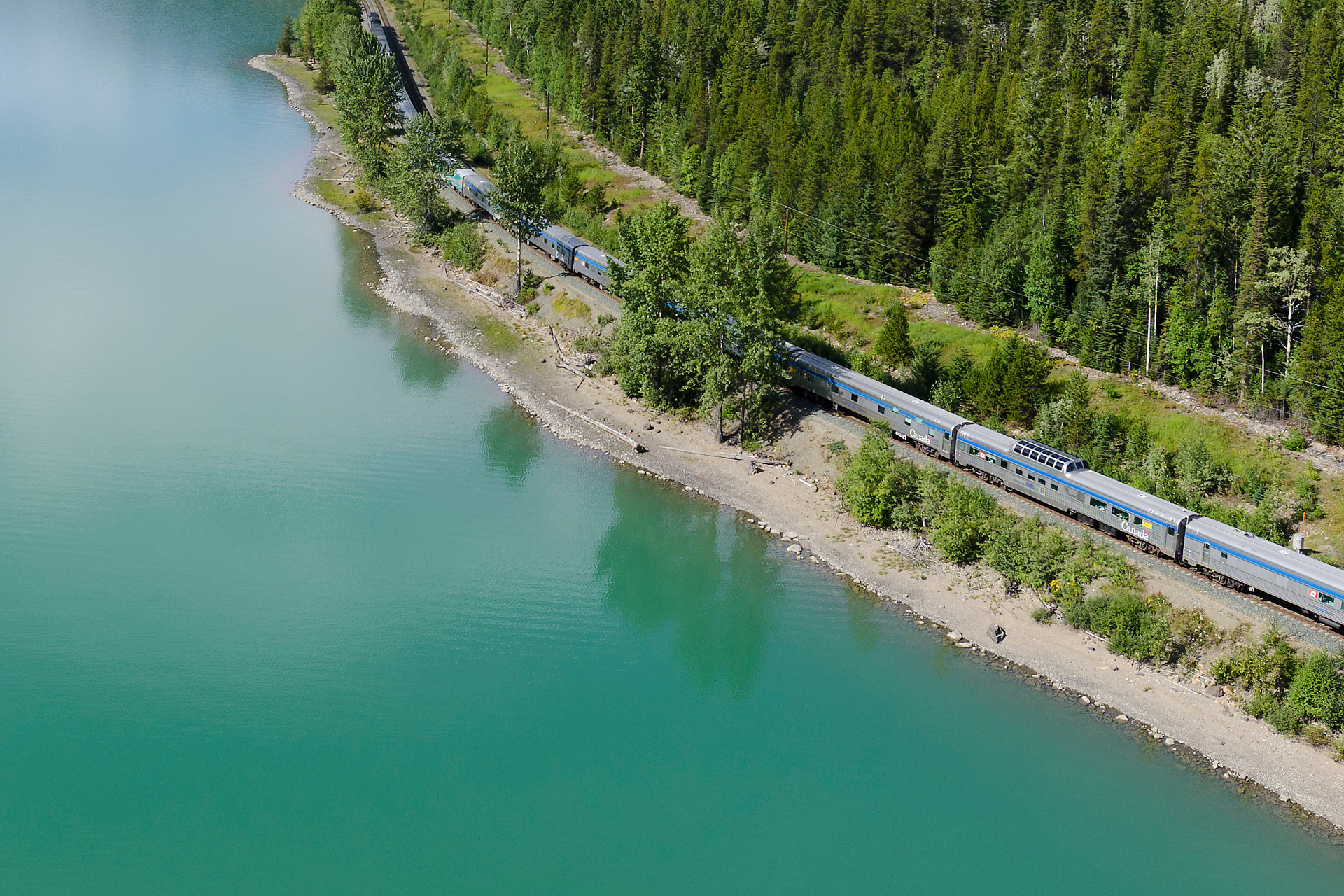 VIA Rail train winding past a turquoise lake and forest