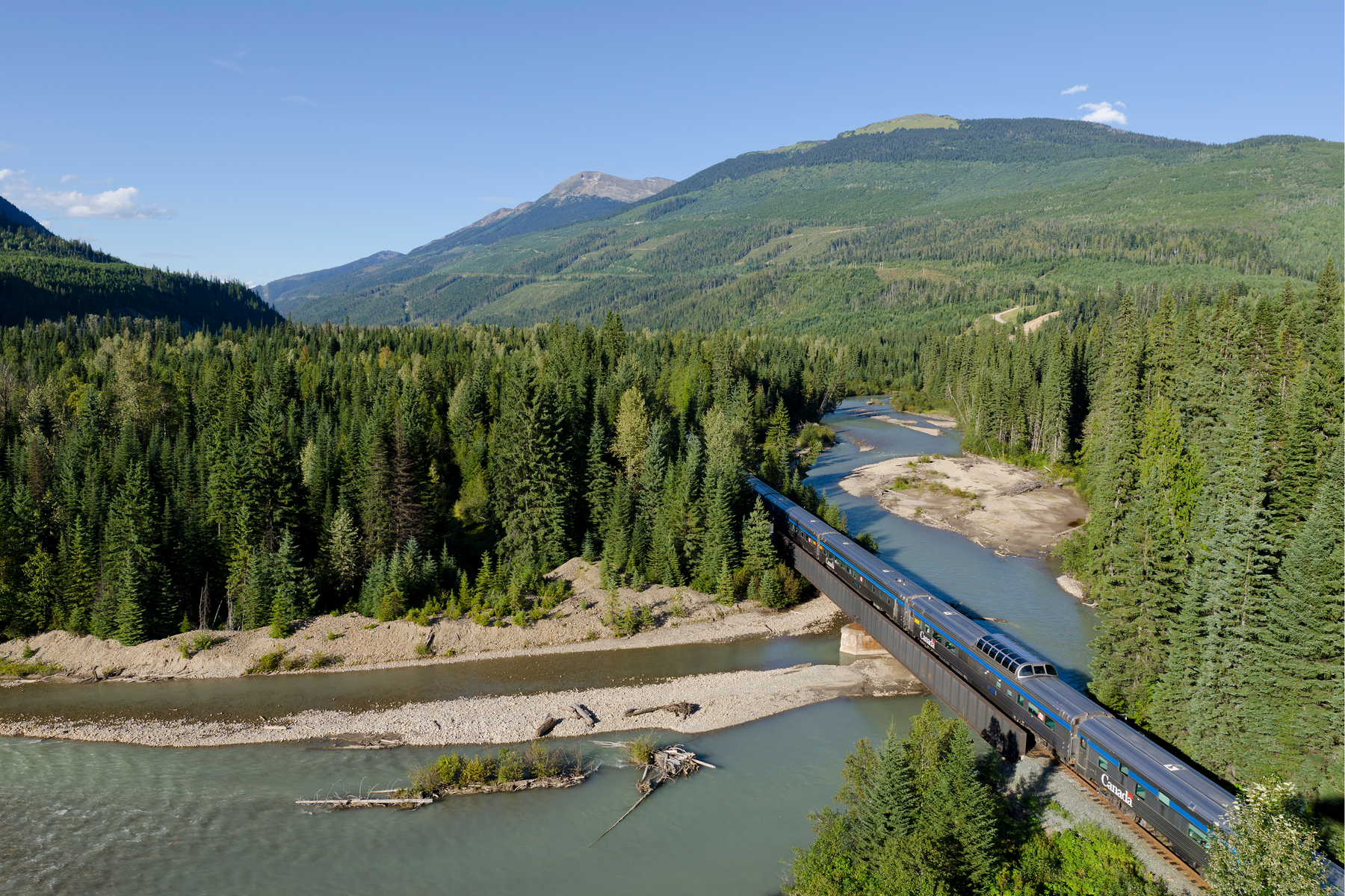 VIA Rail train in between a lake and trees in the Canadian Rocky Mountains