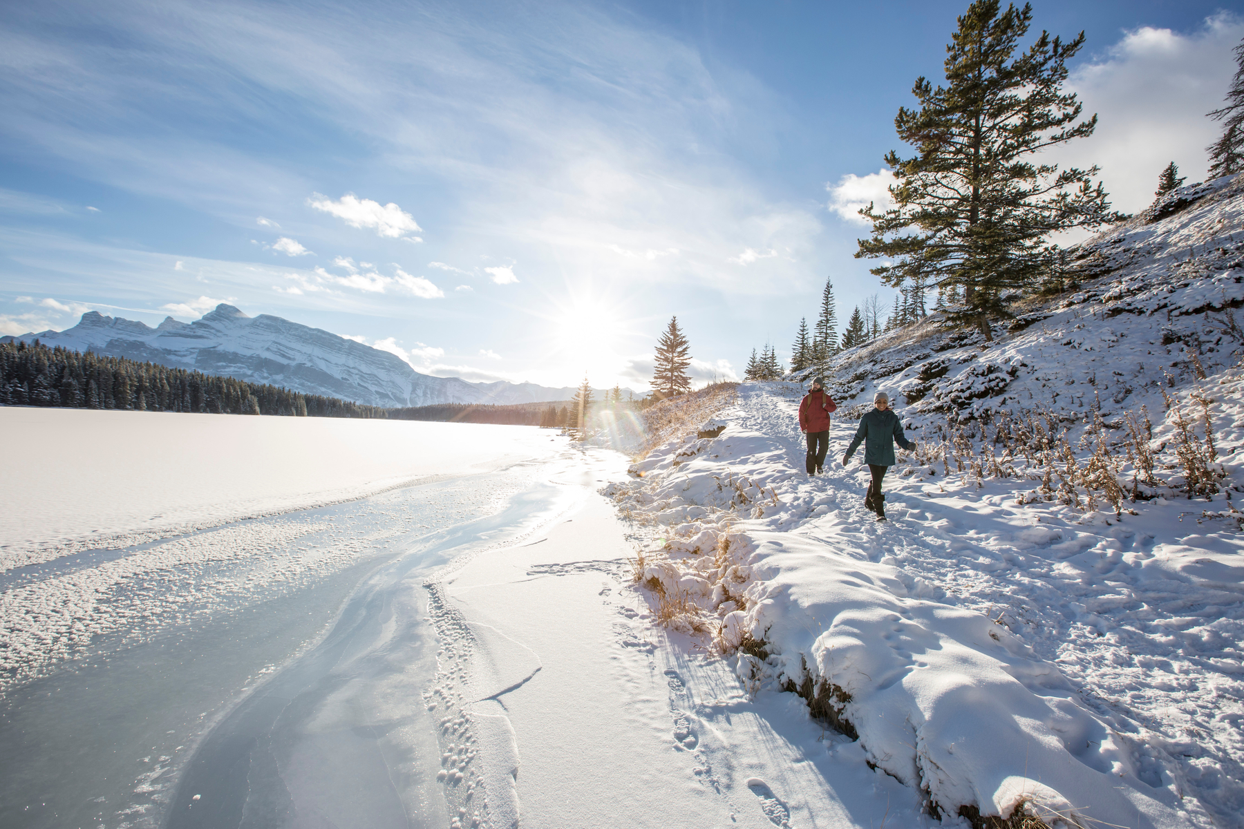 Two people walking in the snow beside the icy Two Jack Lake in Banff