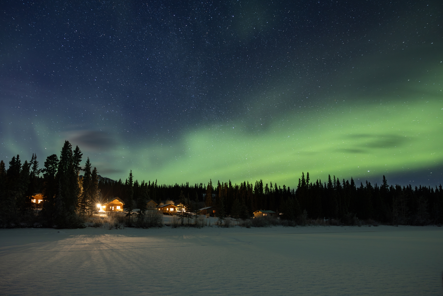 The Northern Lights glow in the sky above cabins at Southern Lakes Resort in winter