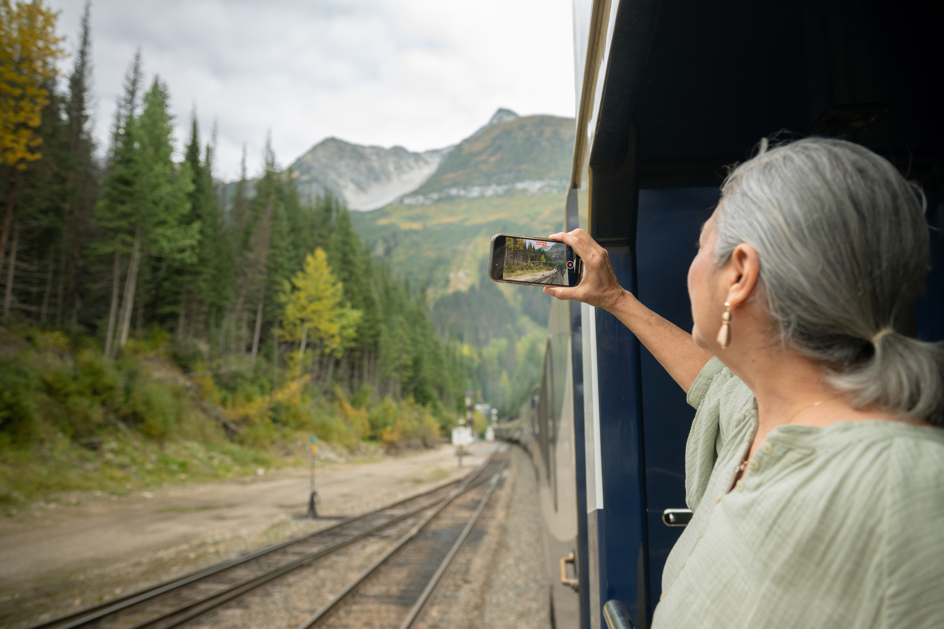 Guest taking photo of tree scenery from outdoor viewing platform on the Rocky Mountaineer Train
