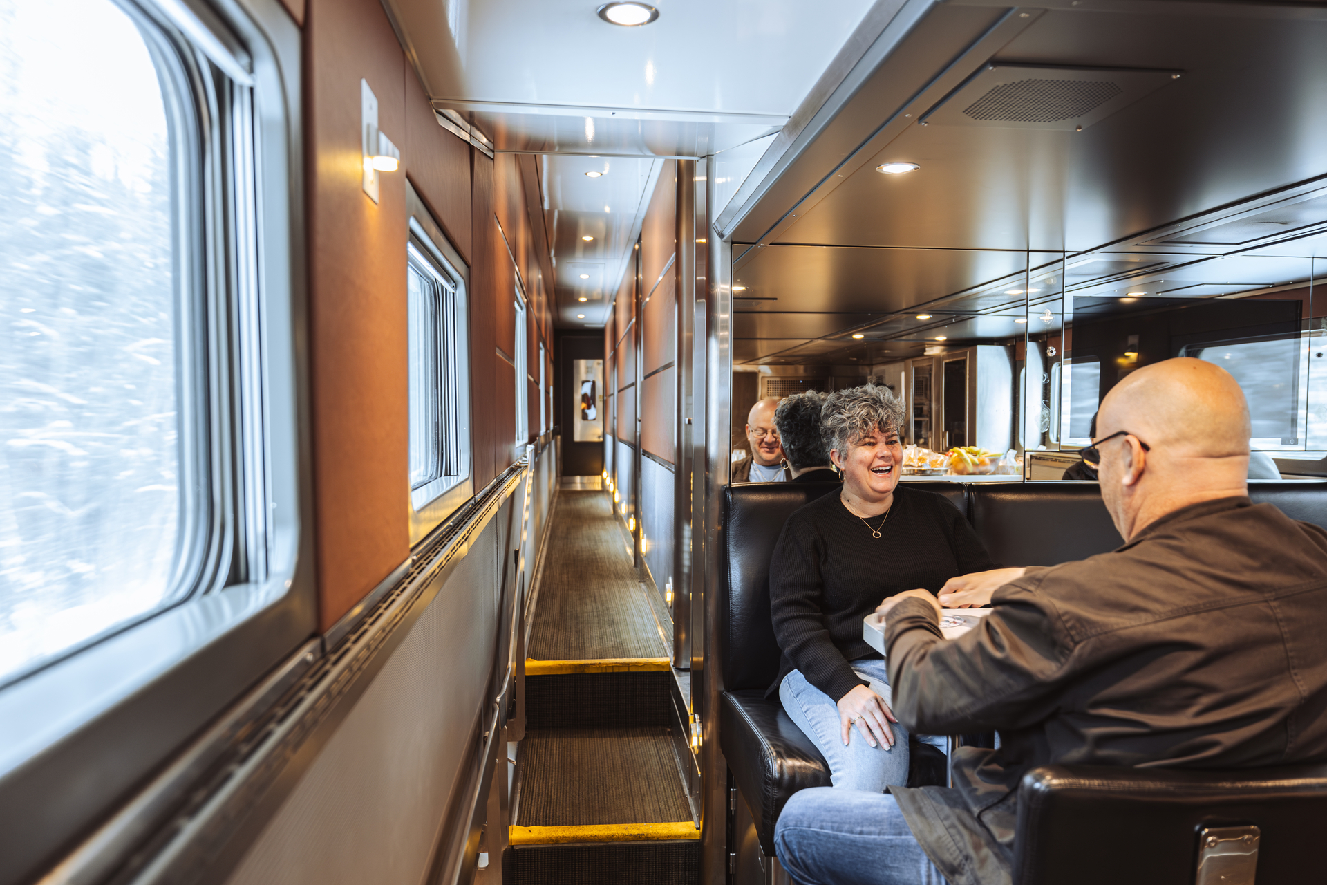 Seated passengers interact in Prestige Park car Mural Lounge onboard VIA Rail's train, The Canadian, during winter