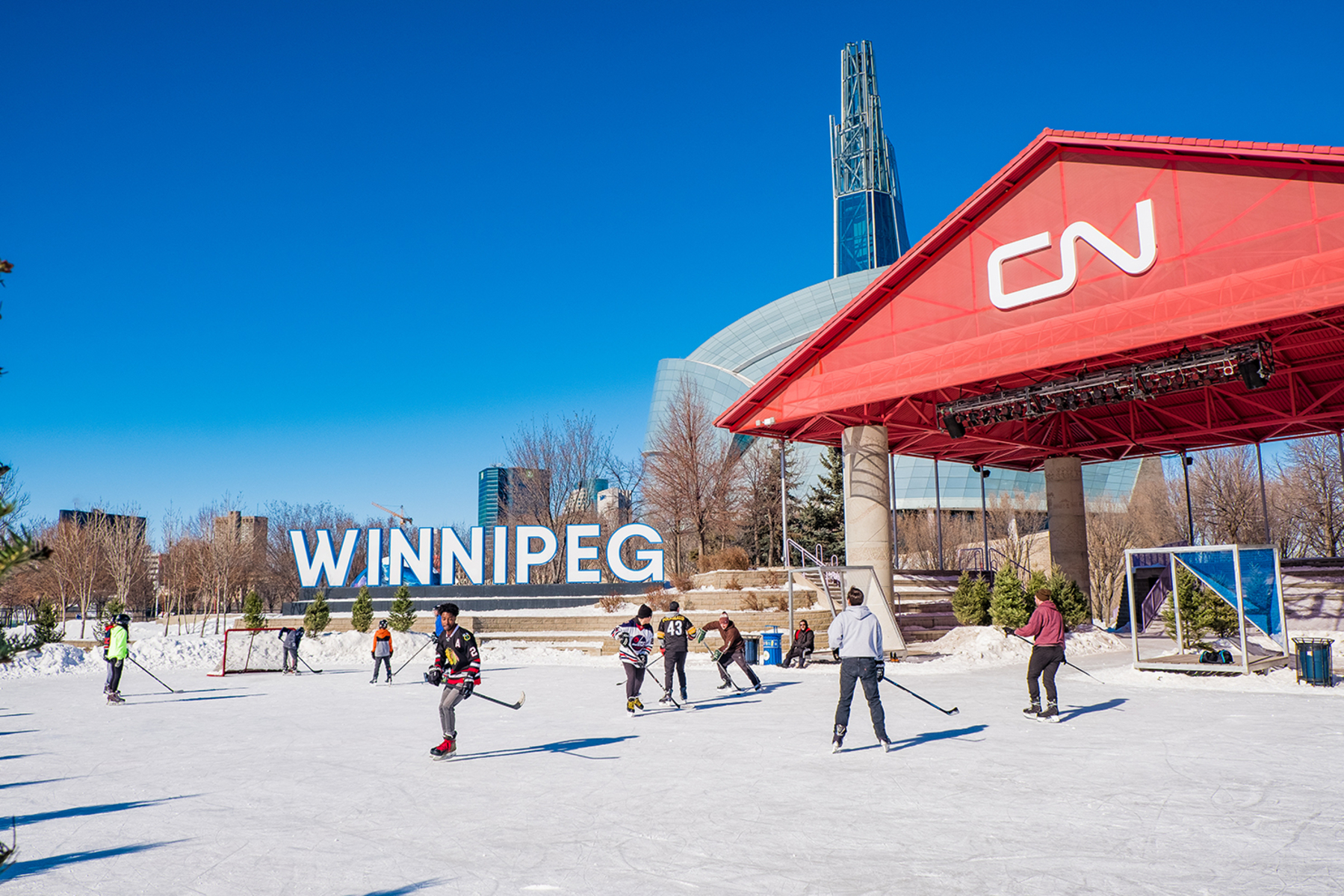 People playing ice hockey on an outdoor ice rink by the CN stage and Winnipeg sign