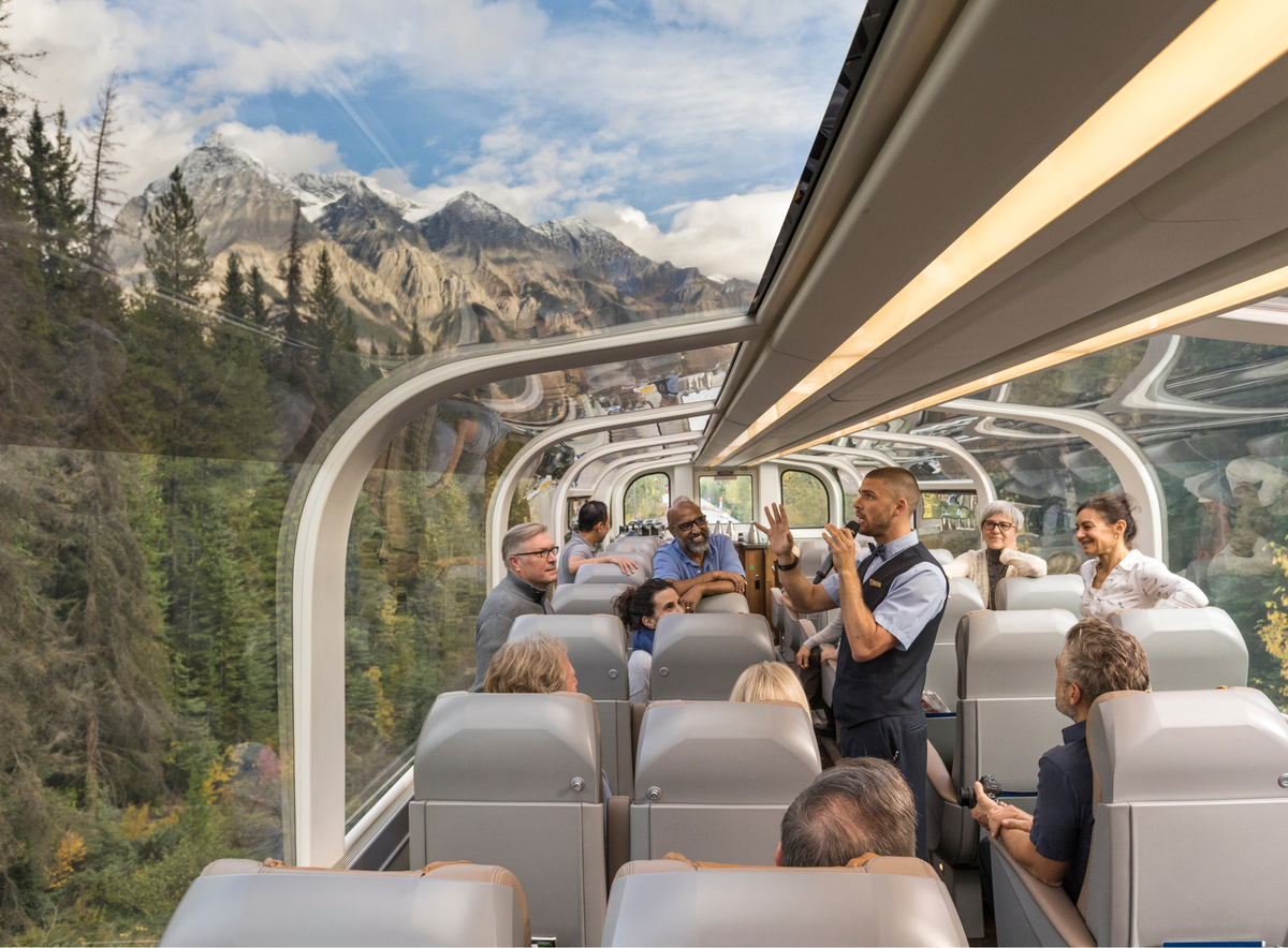 Host talks about the scenery as guests enjoy panoramic views from the glass-dome GoldLeaf coach on Rocky Mountaineer