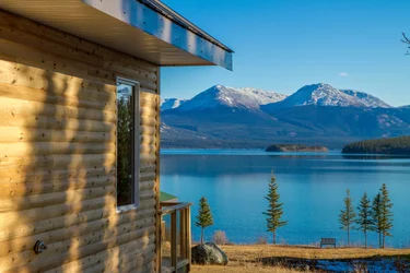 Side of a log cabin with lake and mountains in the distance