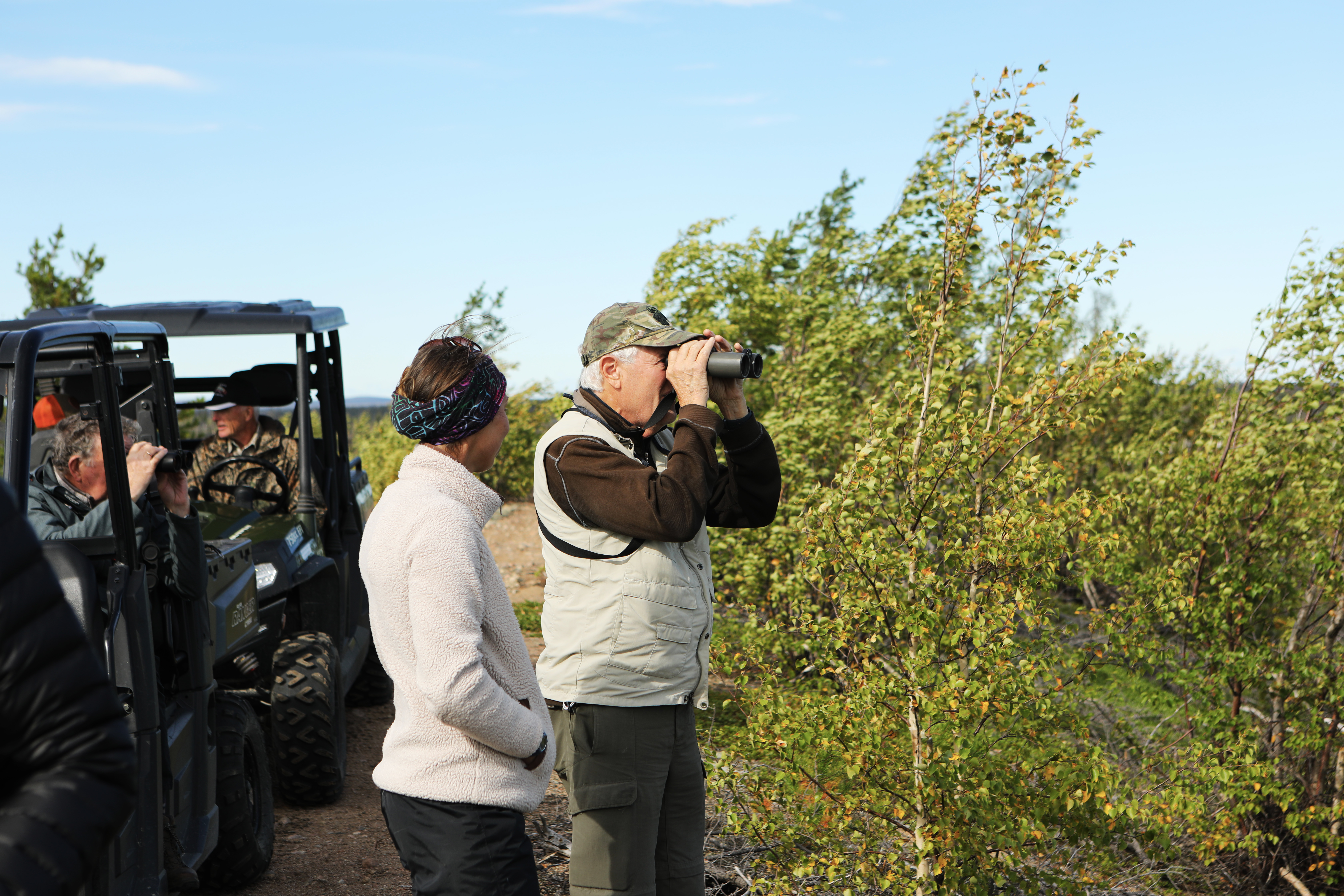 A man is looking through binoculars while standing next to a woman