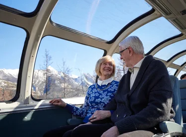 Couple wearing layers and sitting in the domed observation area of VIA Rail The Canadian train to the Rockies
