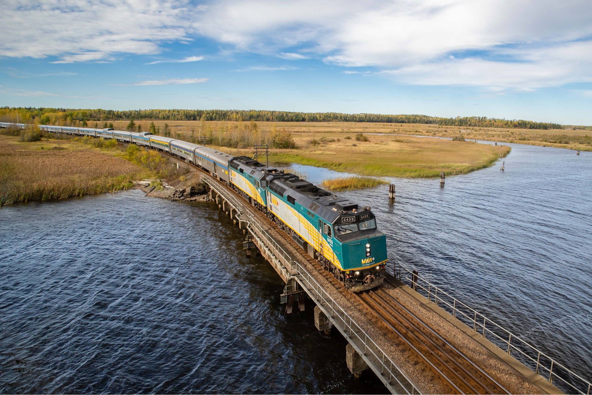 Aerial view of VIA Rail The Canadian train crossing a lake and fields in Ontario
