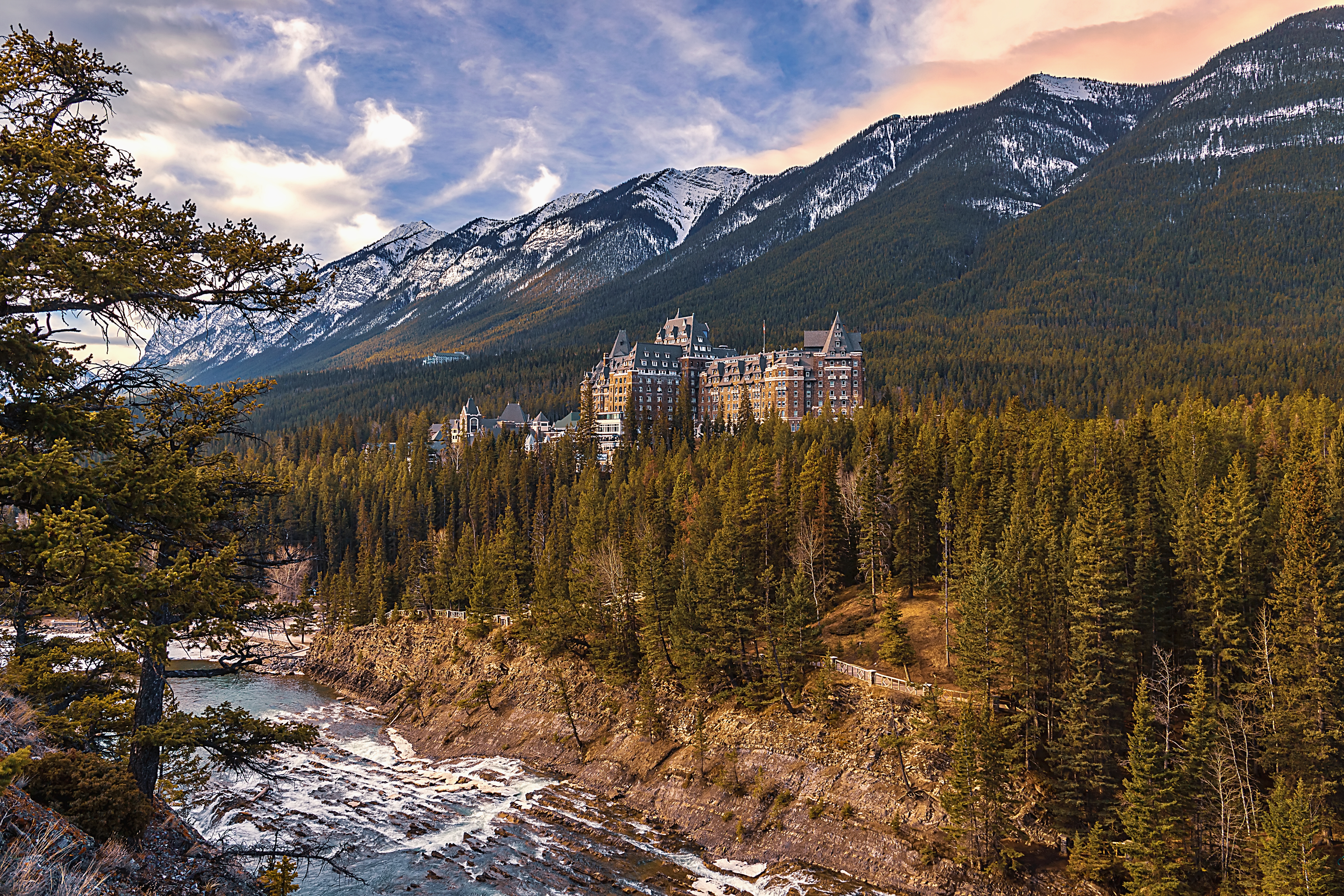 A panoramic view of a cloudy sunrise over mountains and forest by the Banff Springs Hotel.