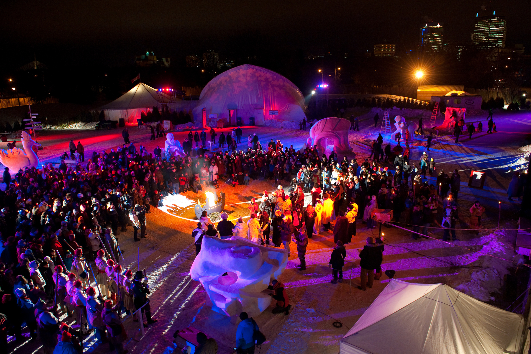 Crowd of people stand around an outdoor show at the winter Festival du Voyageur