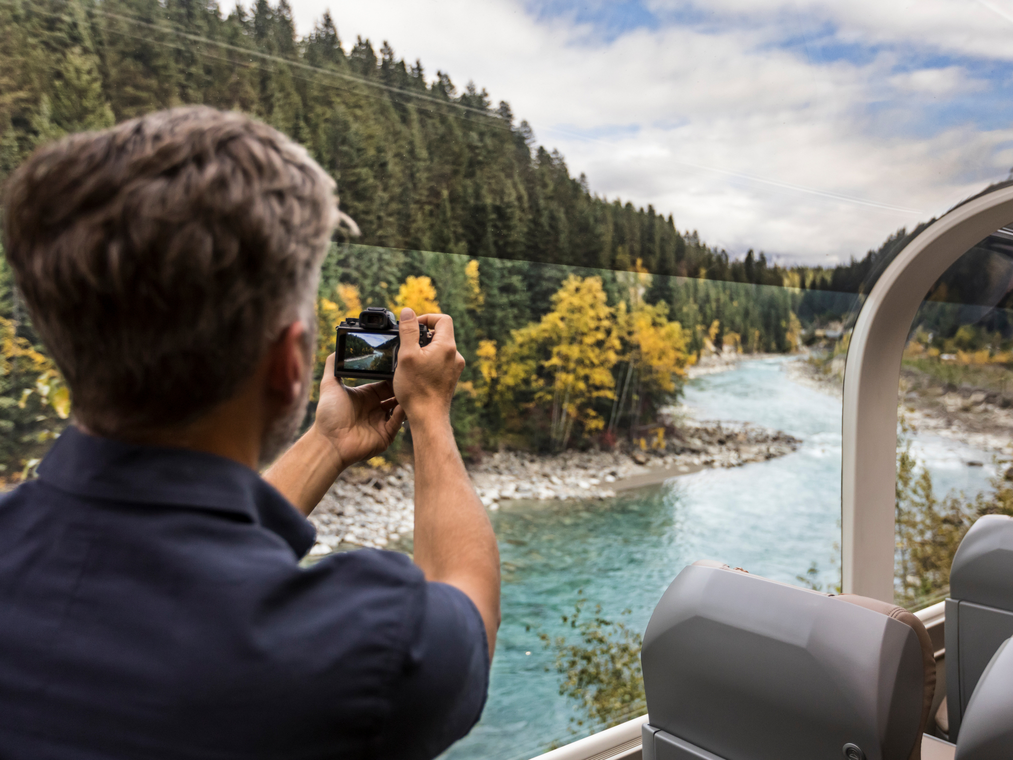 Man takes photo of scenic river from Rocky Mountaineer train car