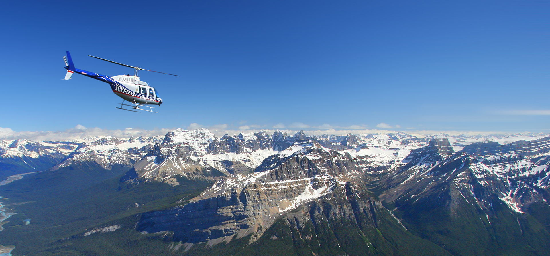 A helicopter flying over the Canadian Rockies on a blue sky day