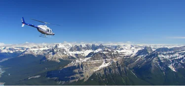 A helicopter flying over the Canadian Rockies on a blue sky day