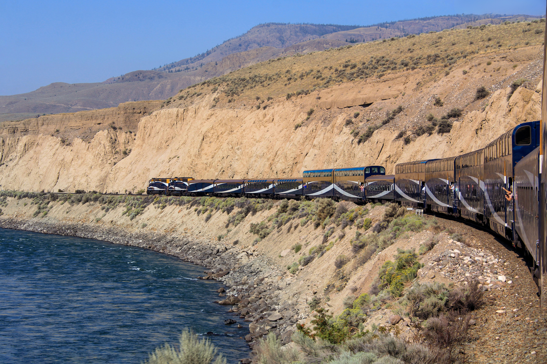 A train traveling on rails alongside the sea near mountains and cliffs