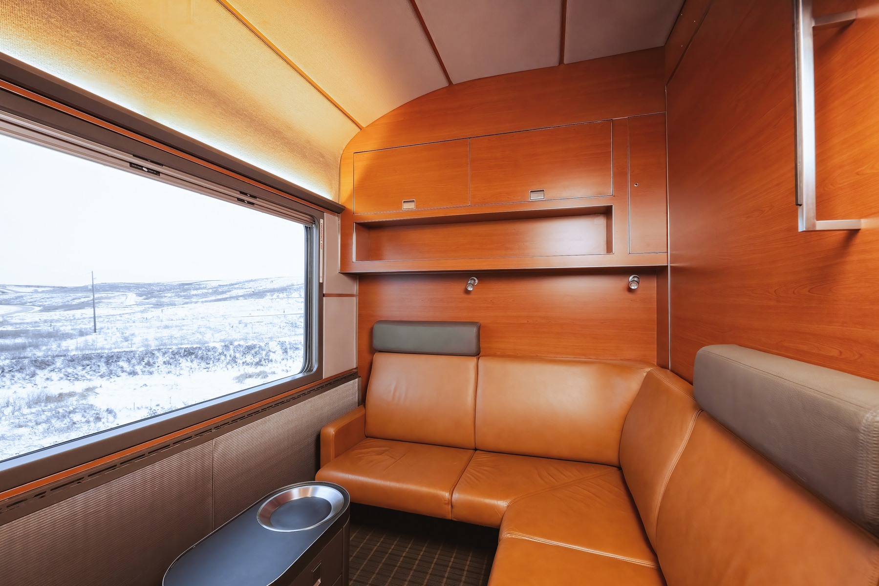 Modular leather couch inside Prestige Sleeper cabin with extra-large window onboard VIA Rail's train, The Canadian, during winter