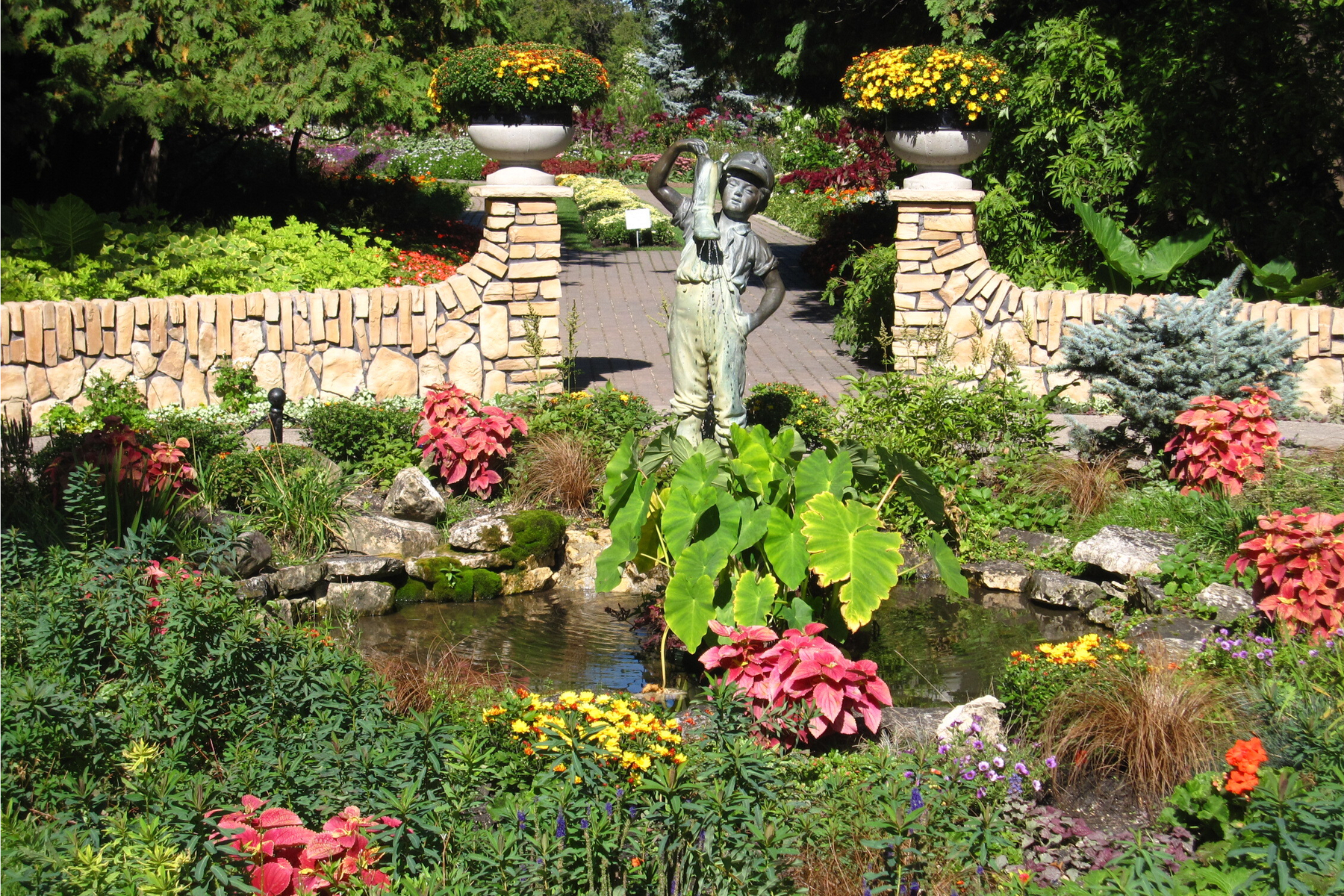 Sculpture of a boy with a boot, flowers and pond in a formal English-style garden