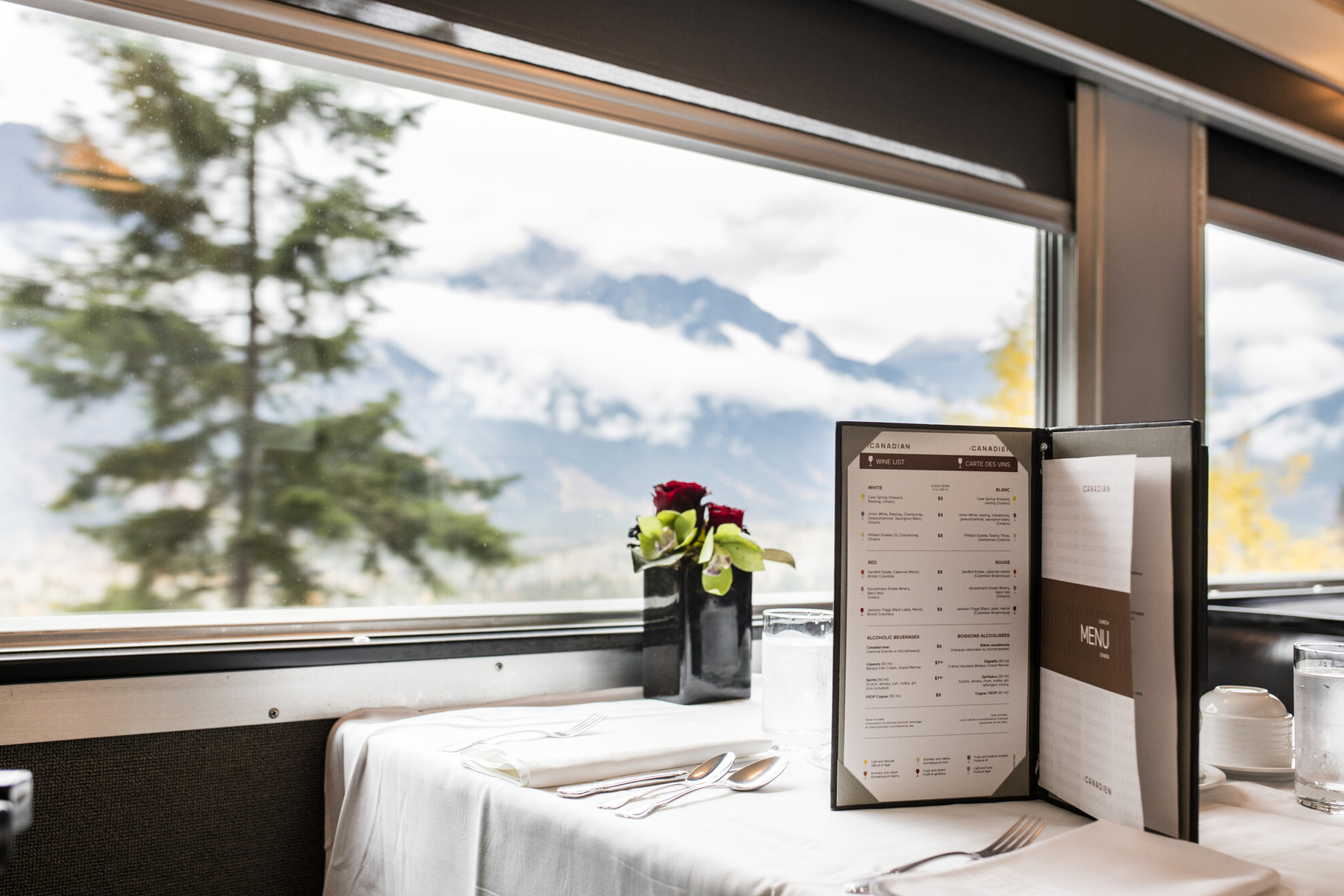 A set table in the train dinig car with an upright menu and flowers.