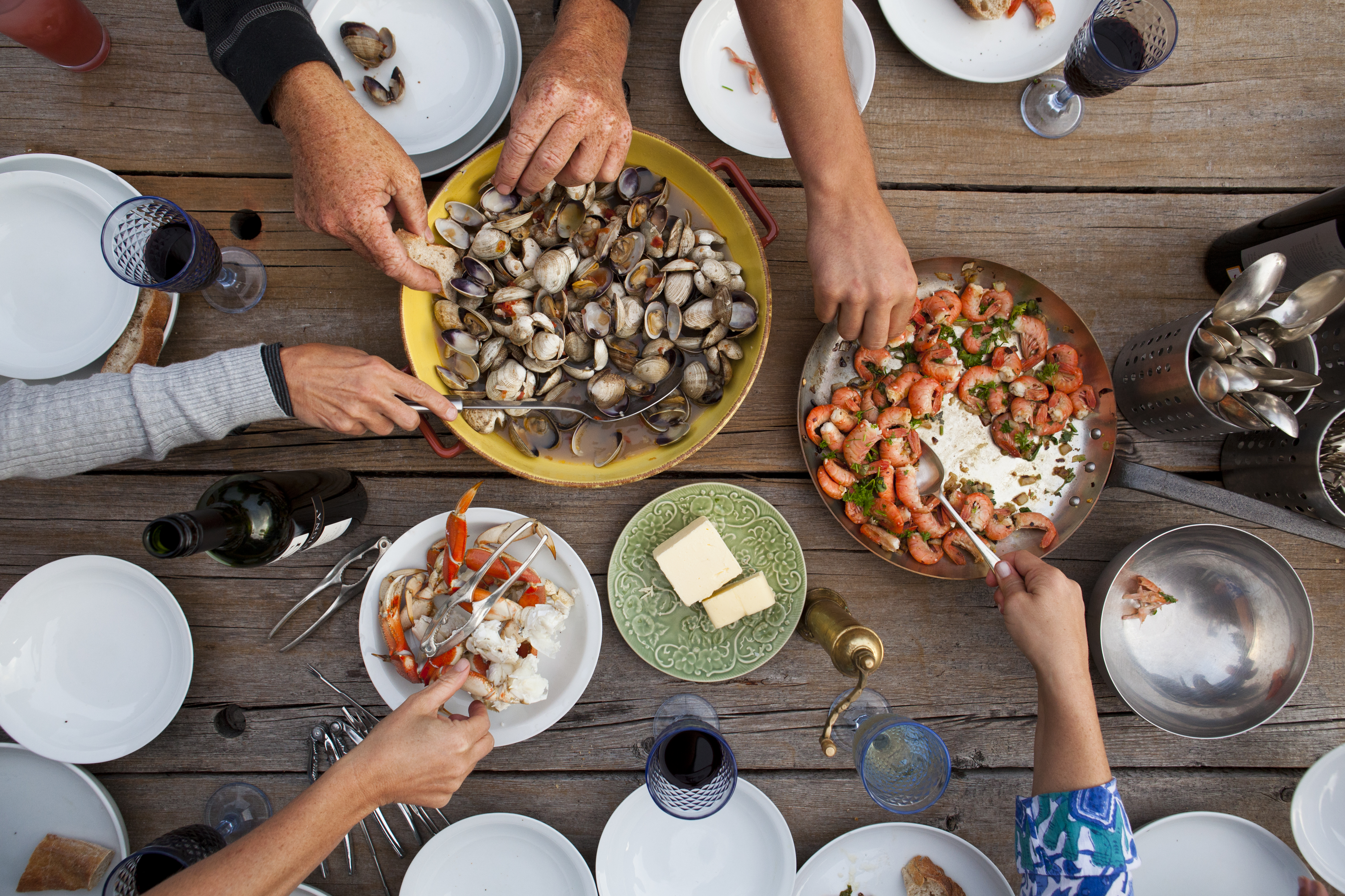 People sharing shellfish like calms, crab and shrimp around a wooden table that showcase hands serving the meal