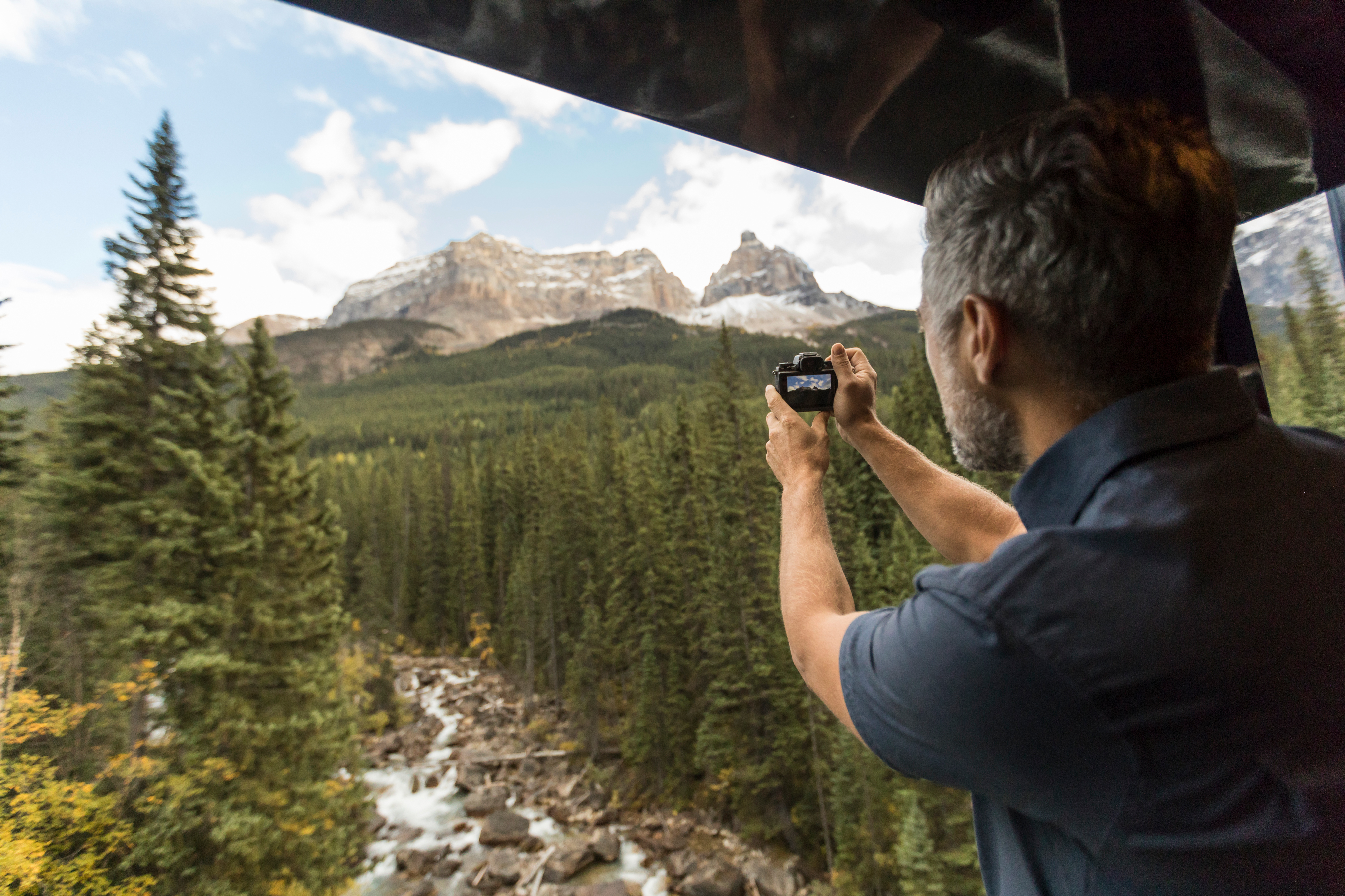 A guest taking a photo of the scenery from the GoldLeaf outdoor viewing platform of the Rocky Mountaineer train