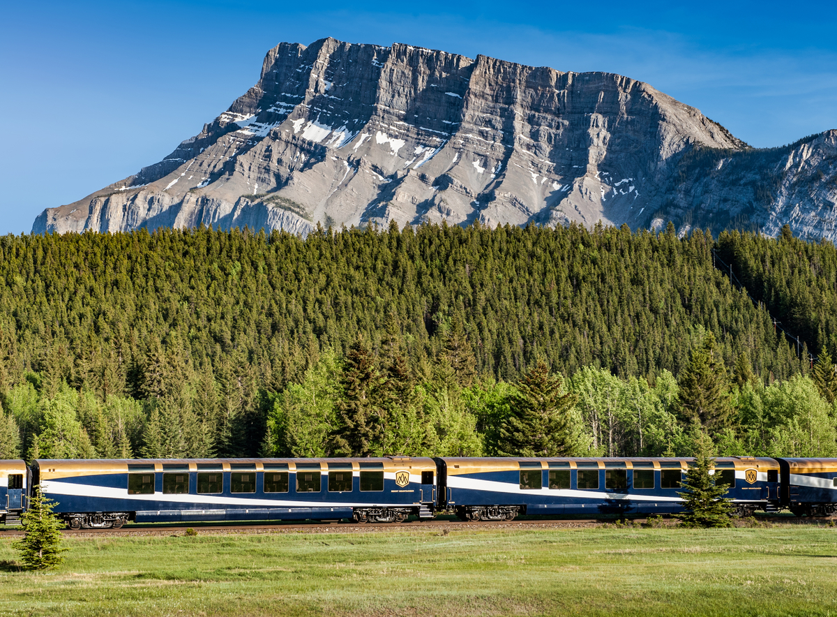 the Rocky Mountaineer train glides past a mountain-backed forest
