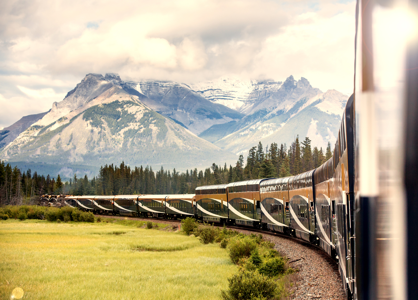 Rocky Mountaineer train rounding a bend in the track with a mountain range in the background.