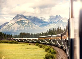 Rocky Mountaineer train rounding a bend in the track with a mountain range in the background.