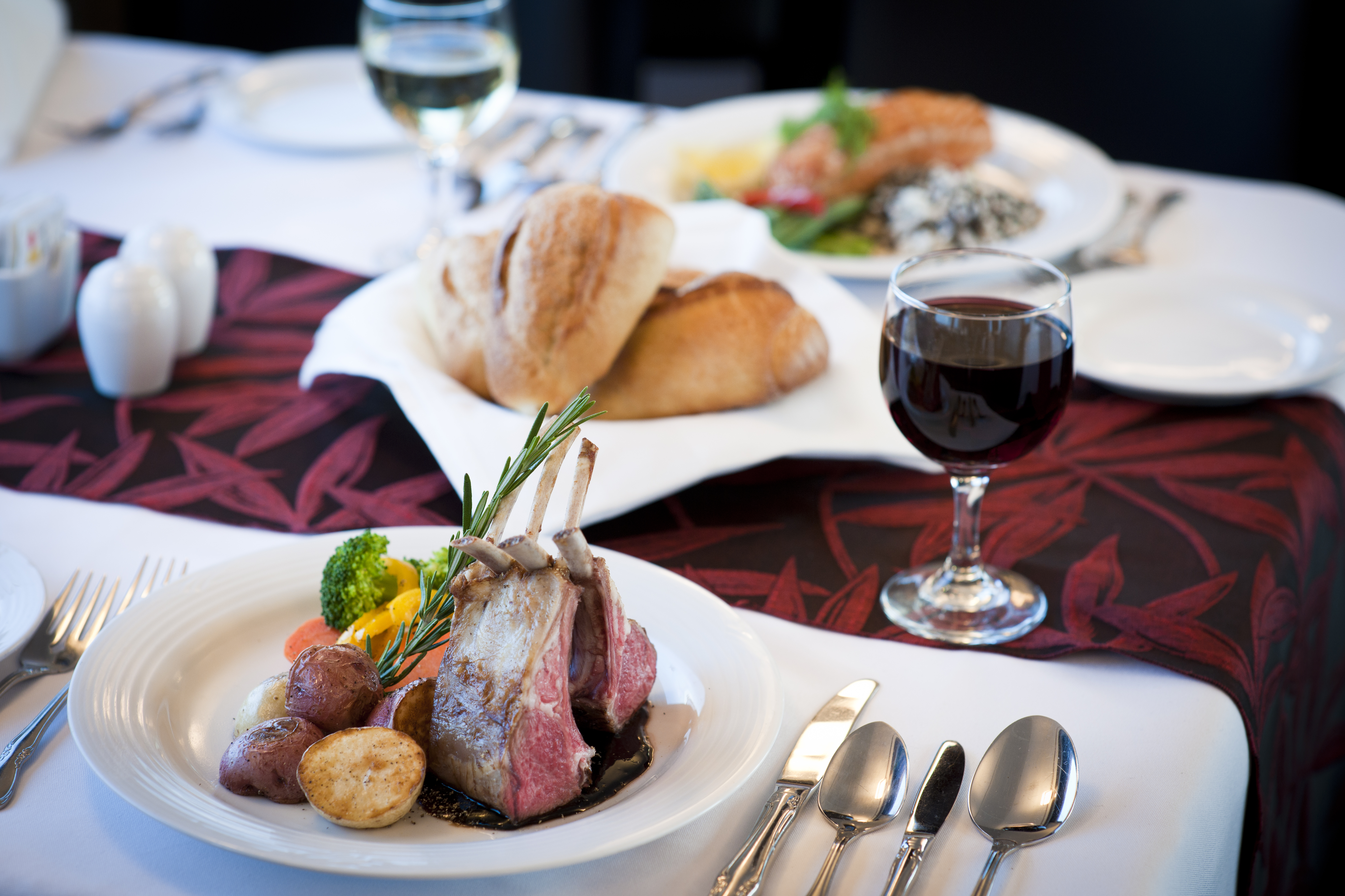 Close-up of a table in the dining car with a lamb entree, salmon entree, two glasses of wine and rolls in the middle.