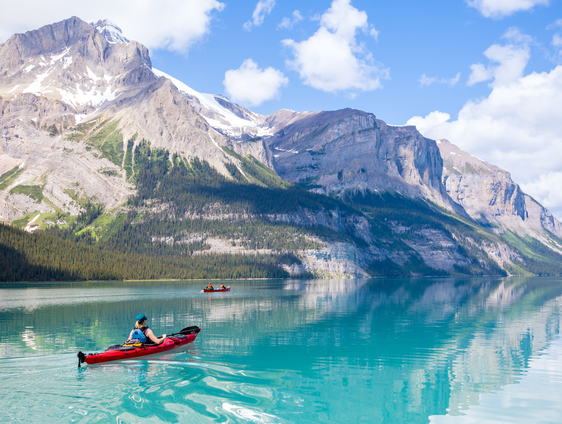 Person paddles a canoe across a lake in the Canadian Rockies in summer.