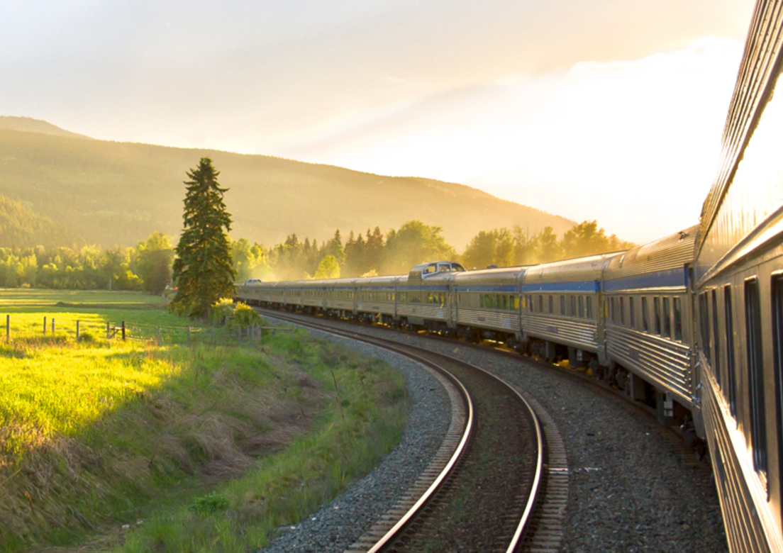VIA Rail train passes green fields at sunset
