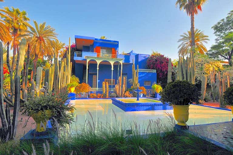Un edificio azul vibrante rodeado de exuberante vegetación y cactus en un jardín.