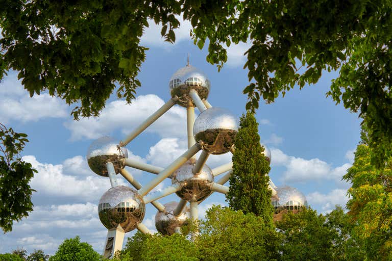 The Atomium in Brussels framed by lush green trees and a blue sky.
