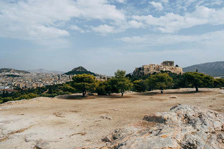View of the Acropolis in Athens with trees and mountains in the background.